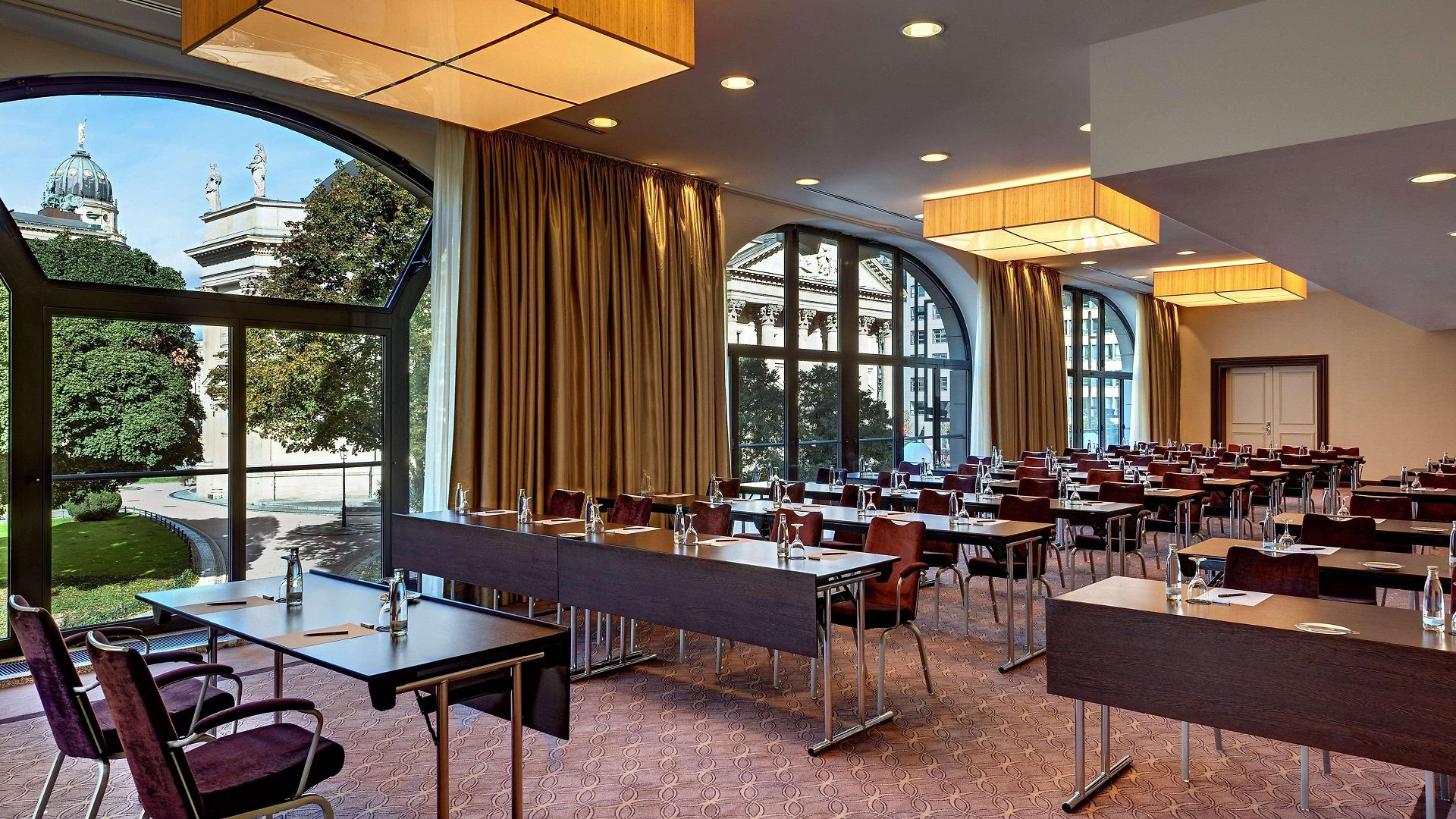 1439595289 Moderne Konferenzräume mit Tischen, Stühlen und großen Fenstern, die auf einen Gartenblick hinausgehen.