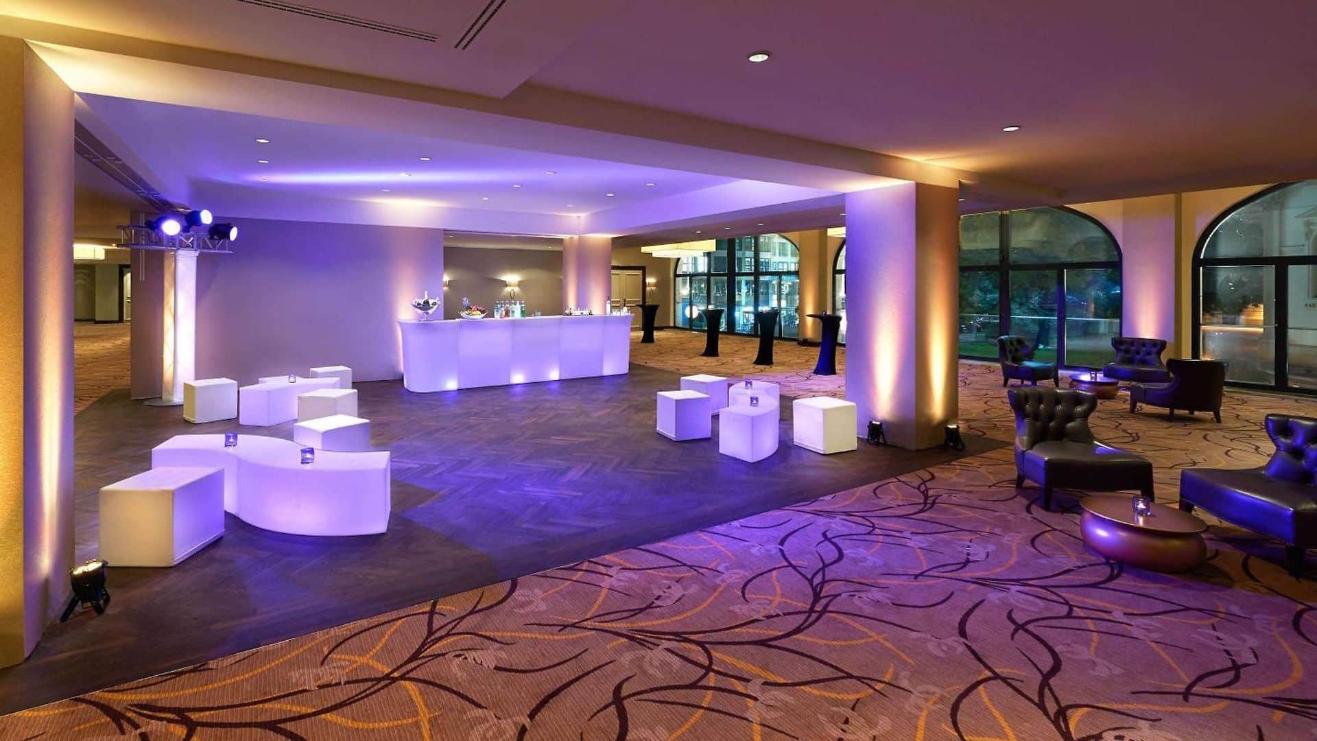 Moderne Eventlocation mit beleuchtetem Empfangstresen, stilvollen Sitzgelegenheiten und sanfter, farbiger Beleuchtung.