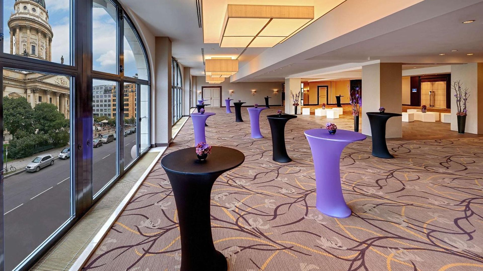 1548869671 Eleganter Veranstaltungsraum mit Stehtischen in Schwarz und Lila, großen Fenstern und Blick auf die Stadt.