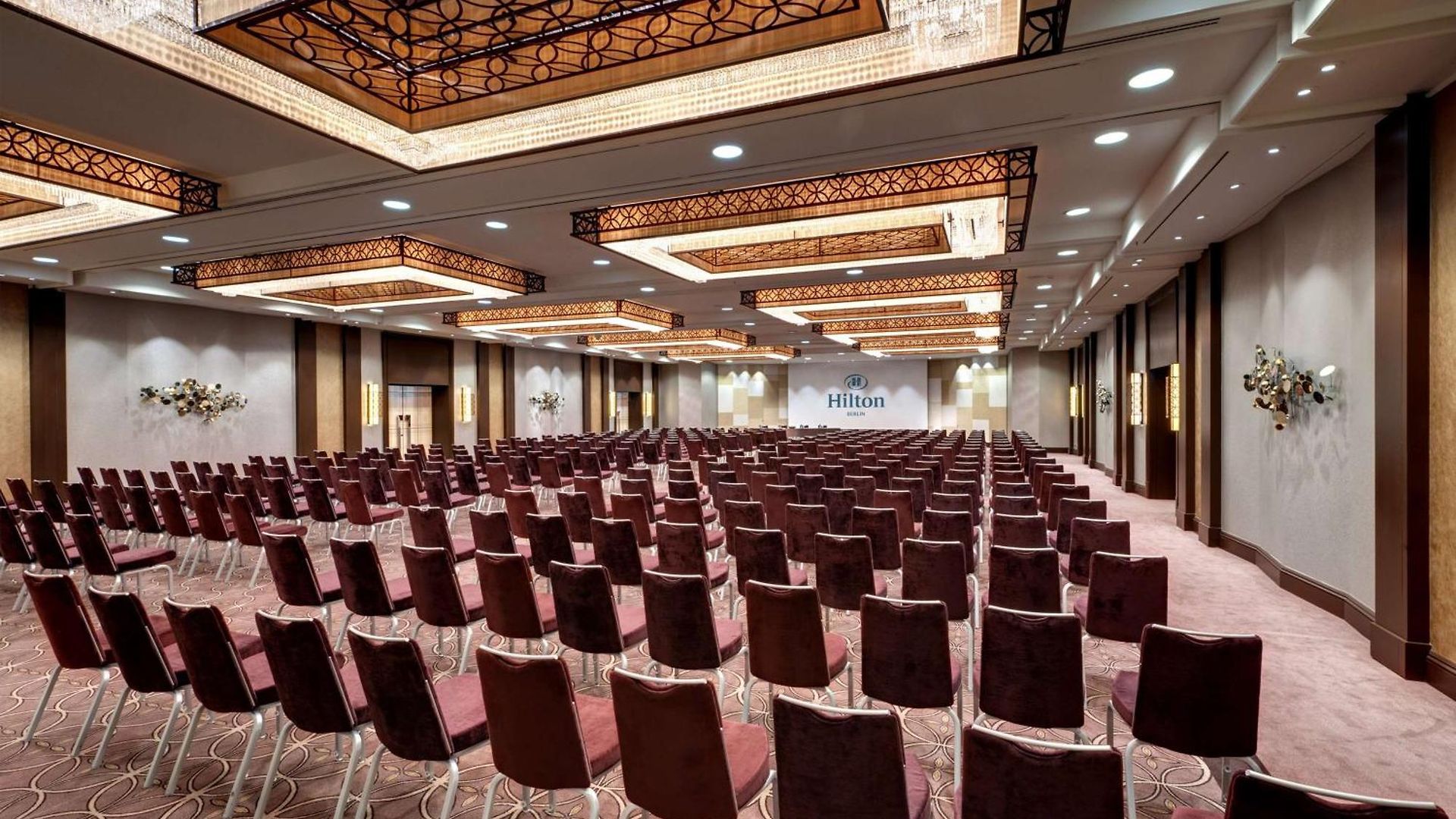 Leerer Konferenzraum im Hilton mit Reihen von Stühlen und dekorativen Deckenleuchten.