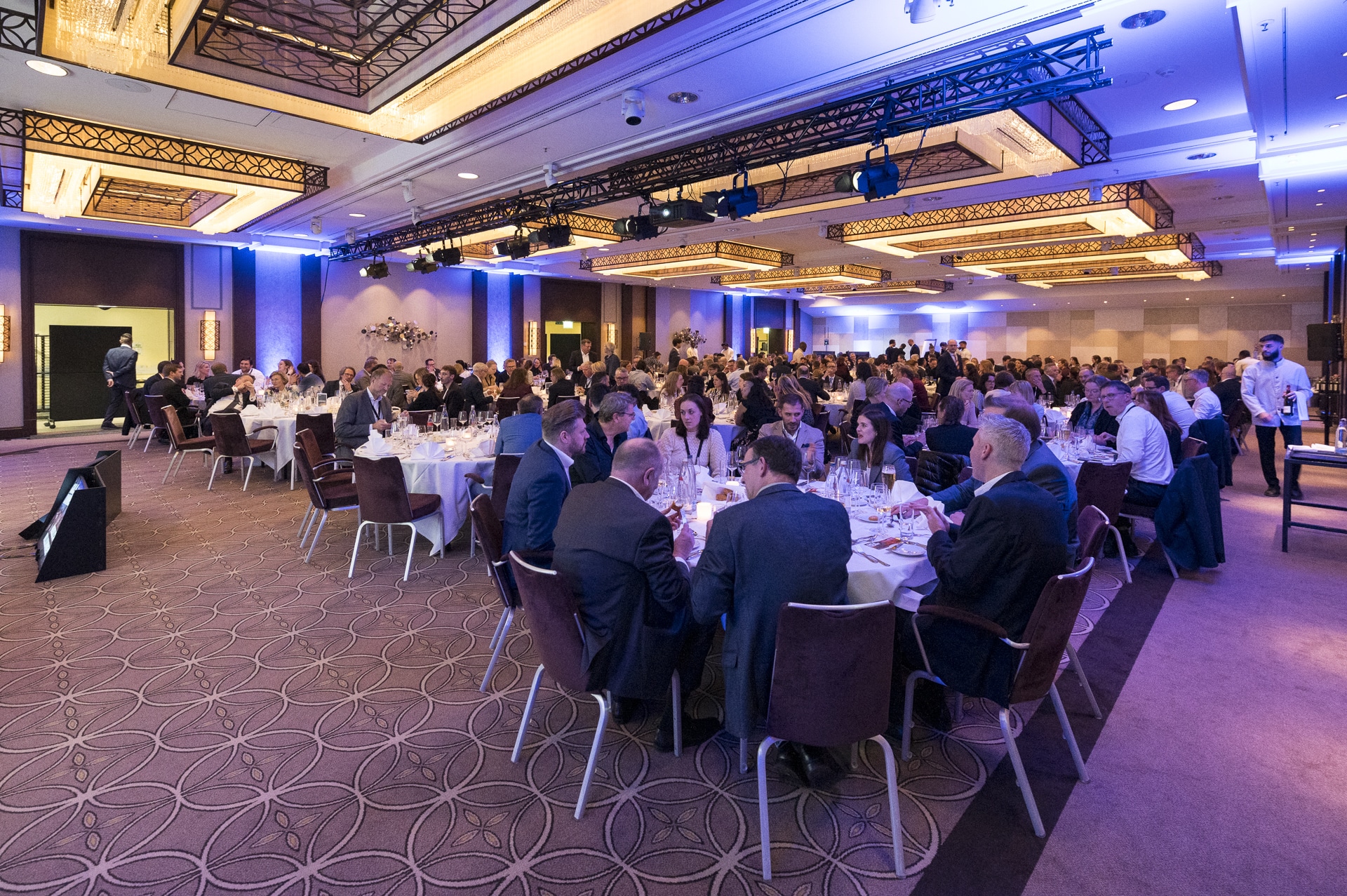 CSebastian Hoehn Große Veranstaltung in einem eleganten Saal mit vielen Tischen, festlich gedeckt und zahlreichen Gästen.