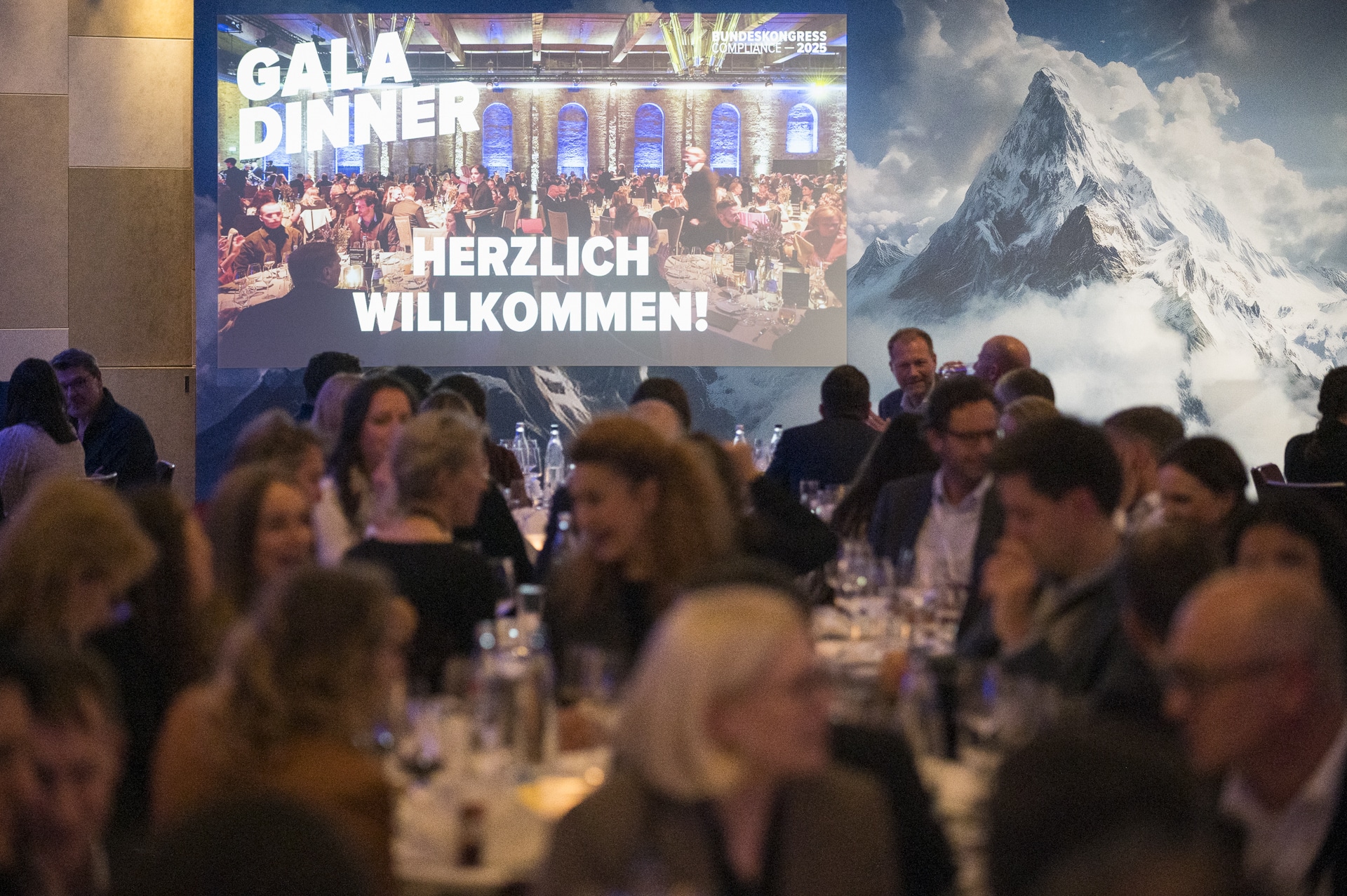 cSebastian Hoehn Gala-Dinner mit festlich gedeckten Tischen und einem Willkommensbanner im Hintergrund, umgeben von Gästen.