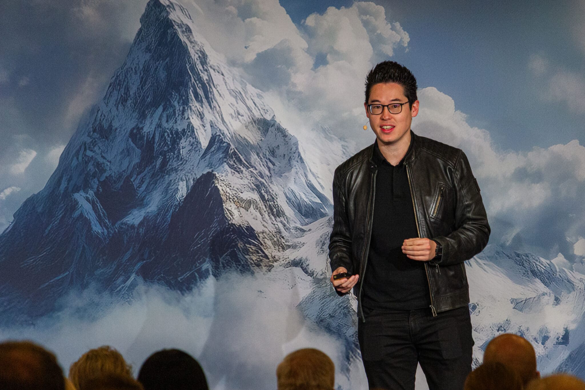 feldmann_robert_8683 Mann mit Brille und schwarzer Lederjacke spricht vor einer Berglandschaft mit Wolken.